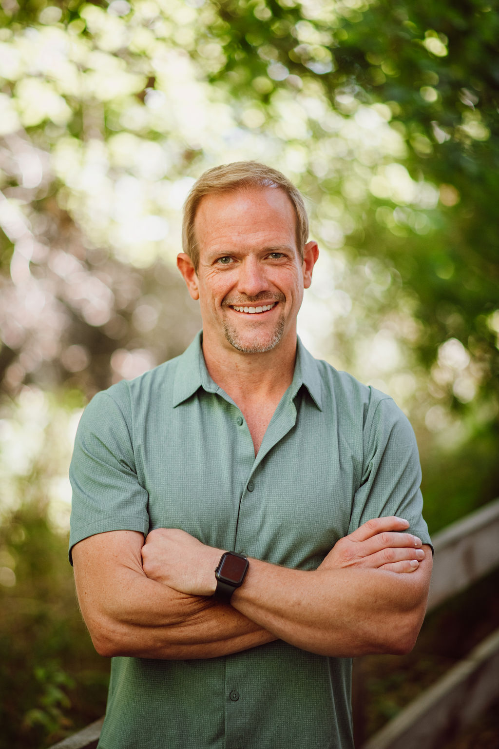 headshot of brillity digital ceo and visionary, derrick kuhn with arms crossed in an outdoor setting, dappled sunlight showing through the blurred background