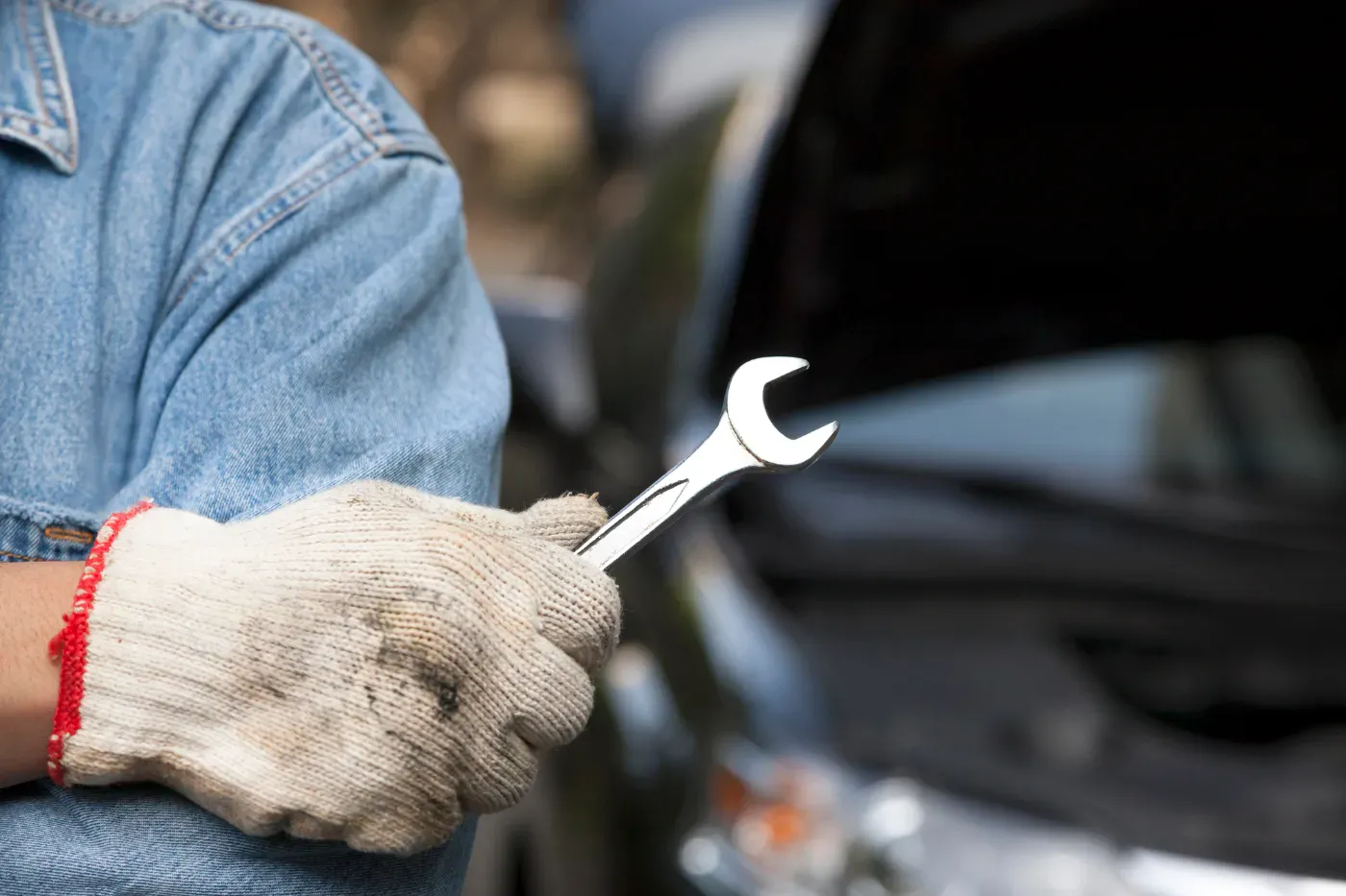 Mechanic holding a wrench beside a car